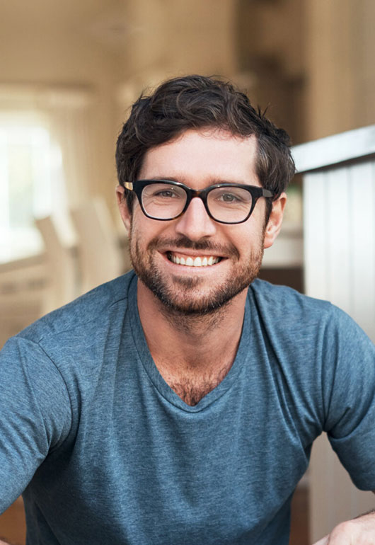 Professional headshot of smiling man wearing glasses and blue shirt in dental office setting.