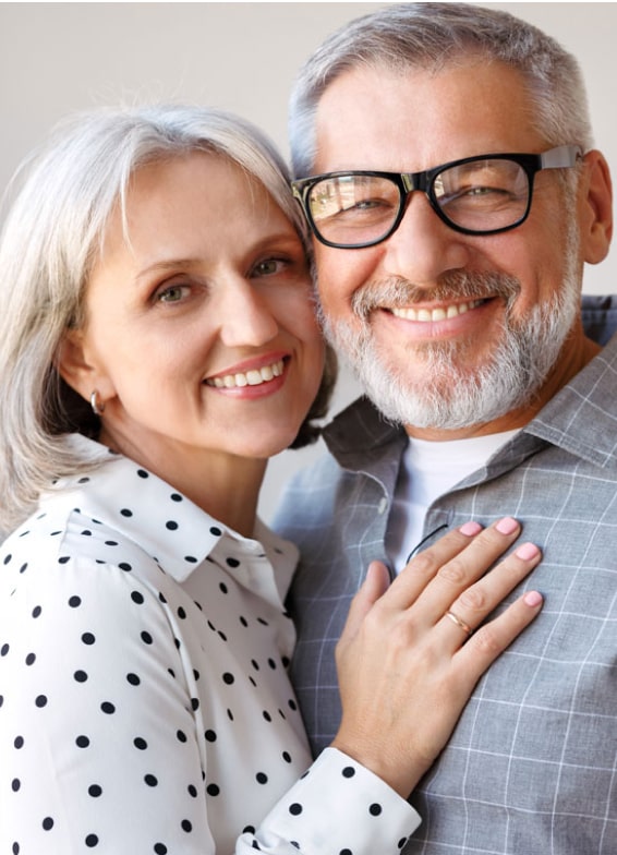 Middle-aged couple smiling together in professional portrait for dental practice website.