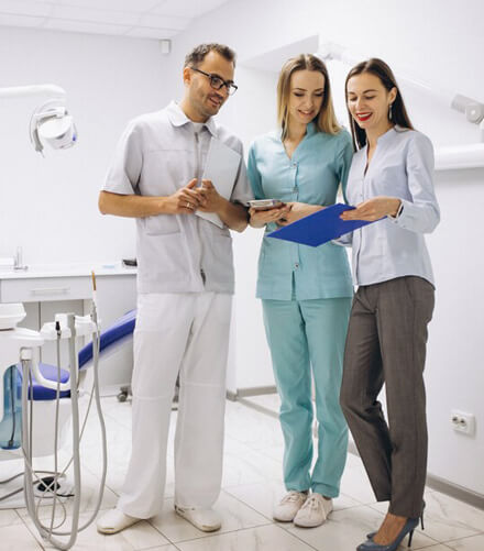 Three dental professionals smiling and holding tablets in a modern dental office treatment room.