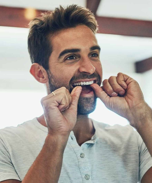 Man flossing teeth in bright dental office setting, demonstrating proper oral hygiene.