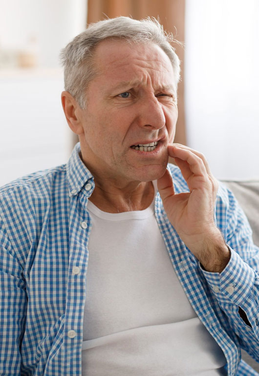 Middle-aged man with hand to face showing dental discomfort in casual home setting.