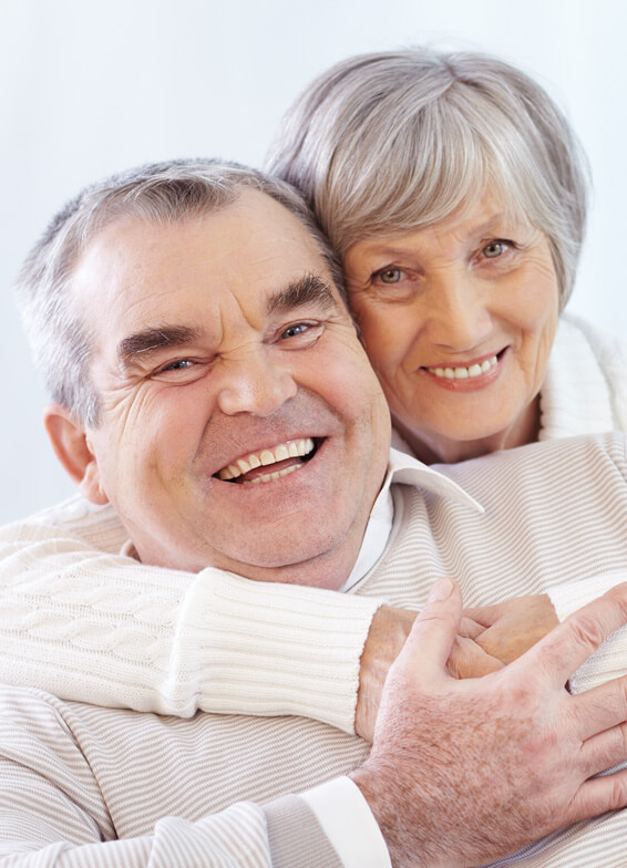 Smiling senior couple embracing in close portrait against white background.