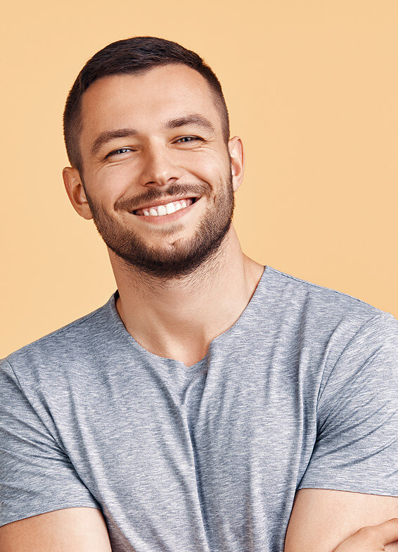 Smiling man in gray shirt against beige background, professional headshot for dental practice.