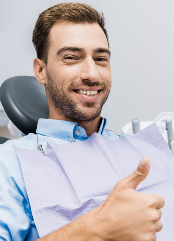 Smiling man in dental chair giving thumbs up in modern dentist office.