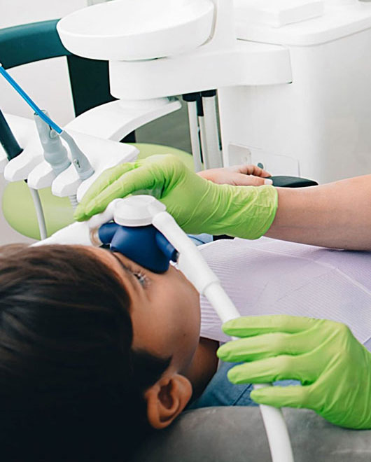 Dentist in green gloves examining patient's teeth in modern dental office chair.