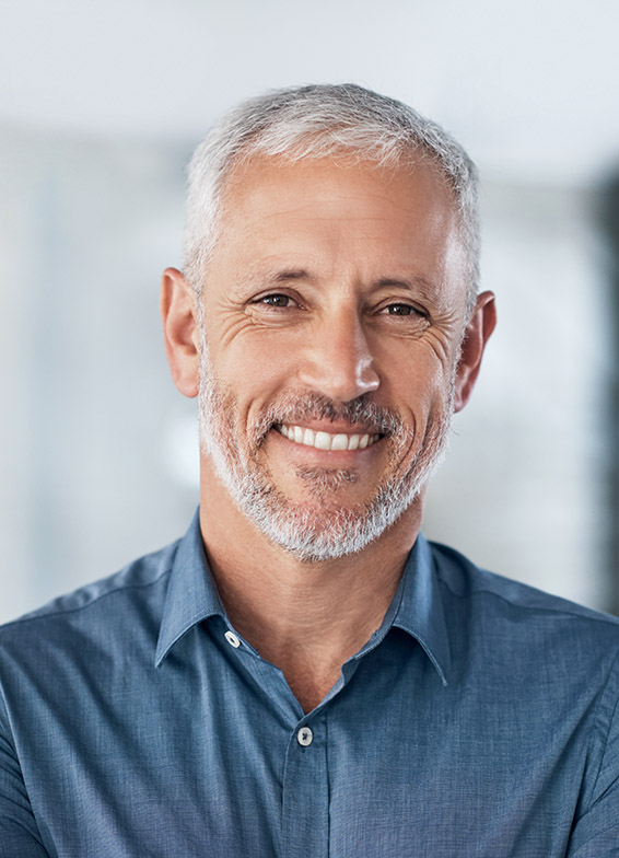 Professional headshot of smiling male dentist wearing blue shirt in modern dental office setting.