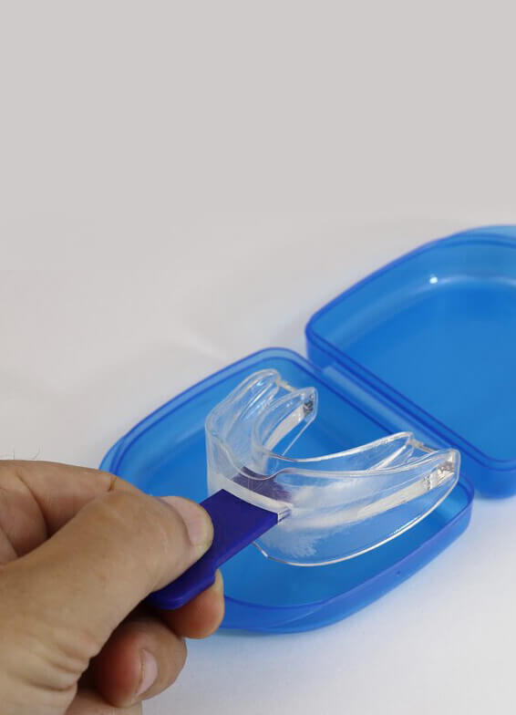 Hand holding clear retainer over blue dental case on white surface