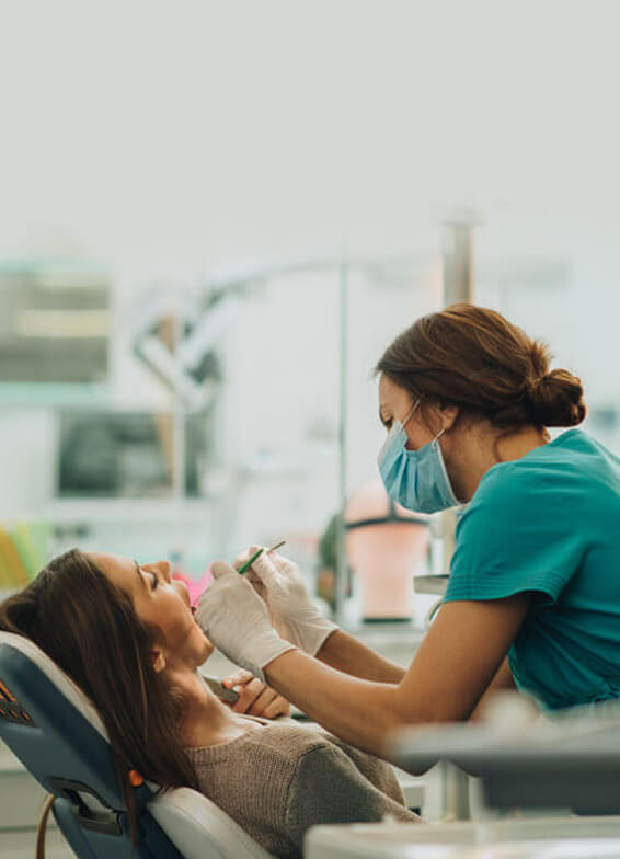 Dentist in teal scrubs examining patient's teeth in modern dental office clinic.