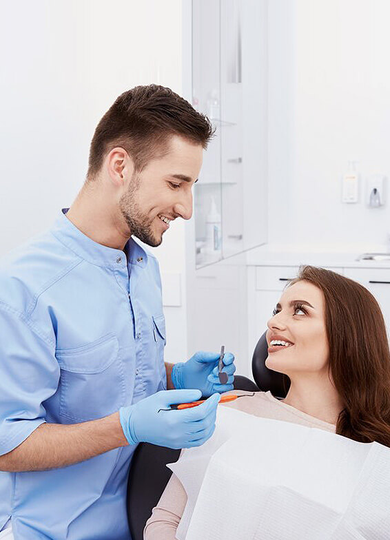 Male dentist in blue shirt examining female patient in dental chair at clinic.