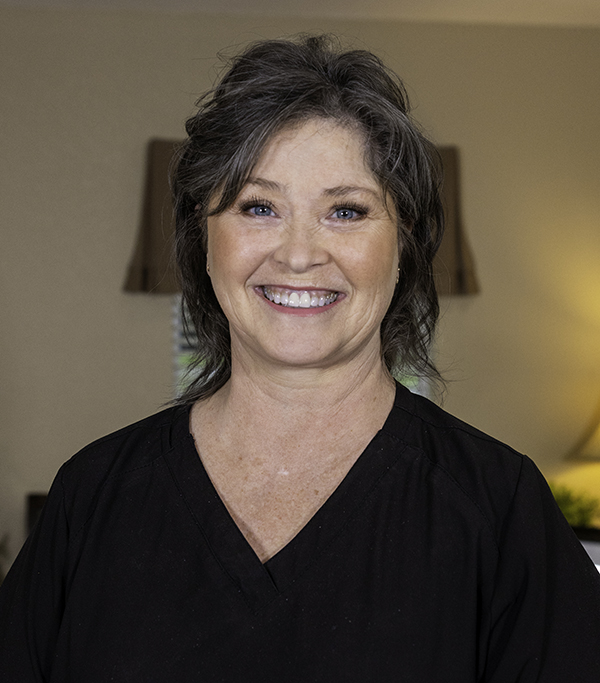 Professional headshot of smiling woman in black top against neutral indoor background.