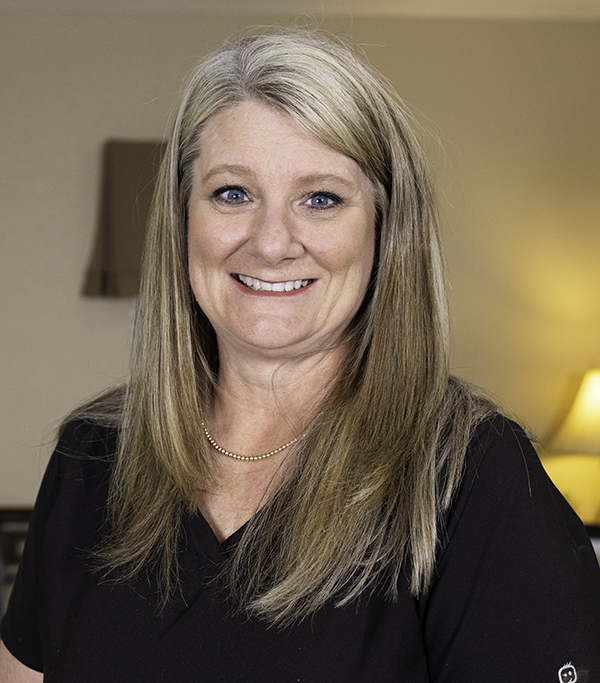 Professional woman smiling at camera in dental office setting wearing black top.