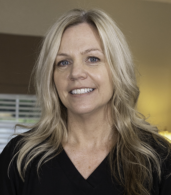 Woman smiling at camera in professional dental office setting with warm lighting.