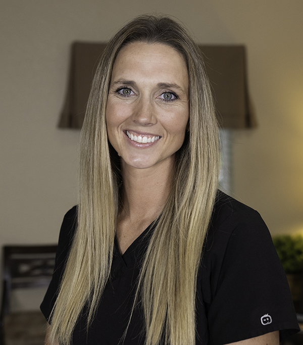 Professional woman smiling at camera in dental office wearing black blazer.