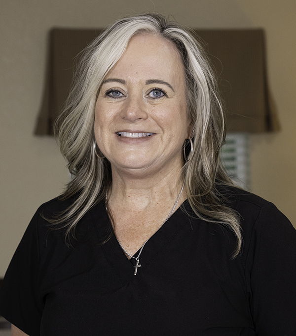 Professional woman with long gray hair smiling at camera in dental office setting.