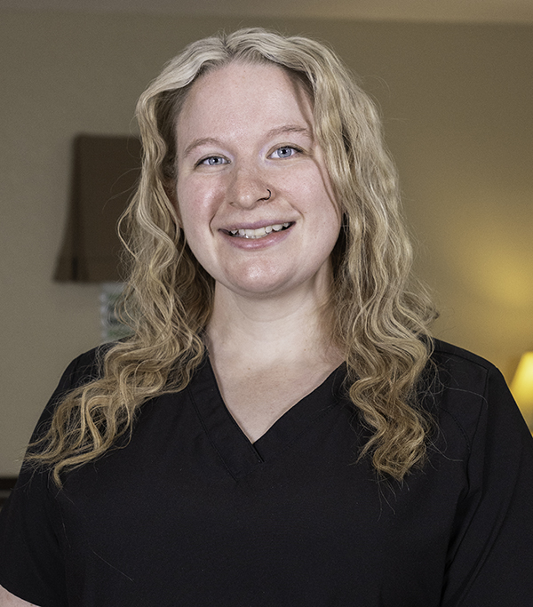 Professional headshot of a smiling woman with blonde wavy hair wearing black, in an indoor office setting.