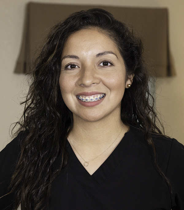 Professional headshot of smiling woman with long dark hair wearing black top against neutral background.