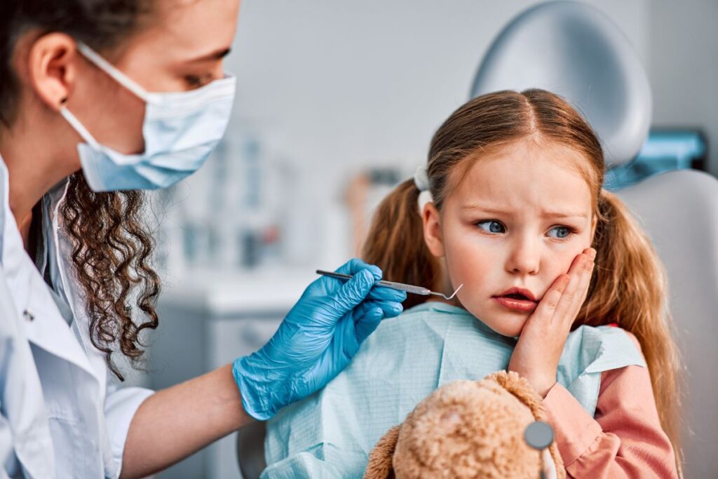 A nervous young girl sits in a dental chair while a dentist gently prepares to examine her teeth.