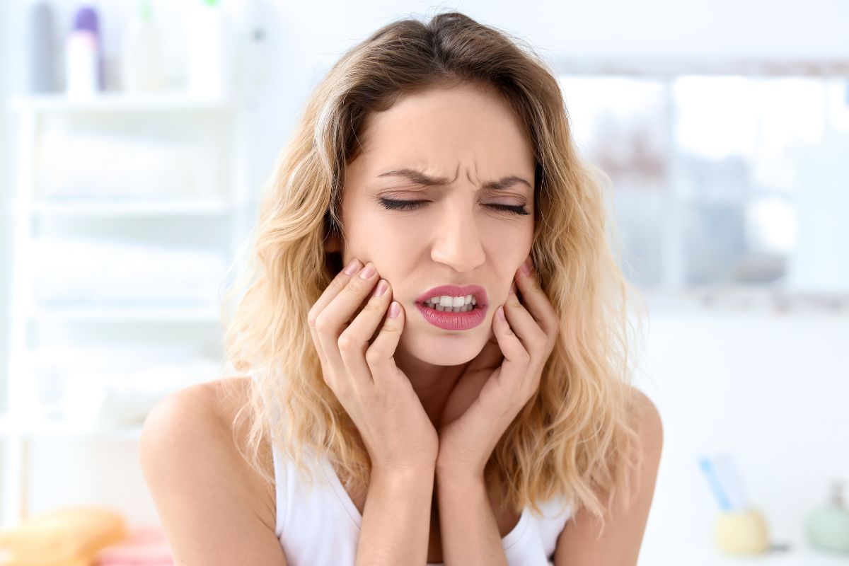 Woman holding her jaw and grimacing in discomfort, illustrating facial pain and muscle tension commonly associated with teeth grinding (bruxism).