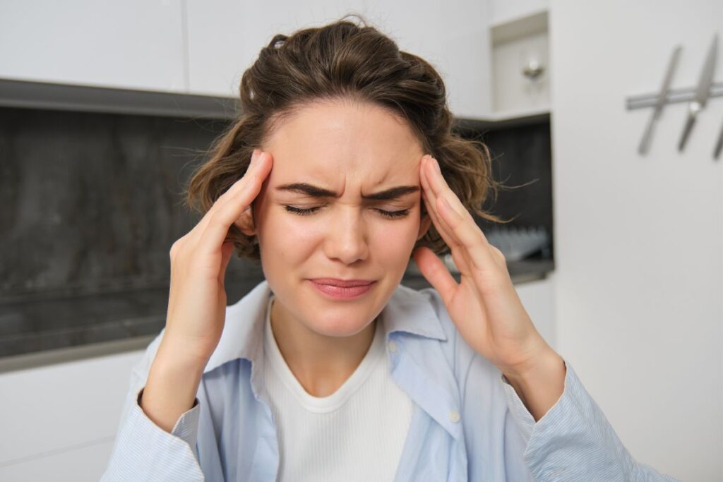 Woman holding her temples and experiencing a headache, illustrating a common symptom associated with teeth grinding, jaw tension, or TMJ disorders.