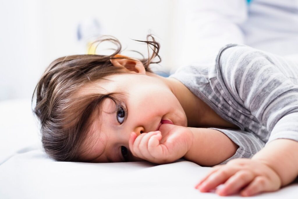 A young child lies on a bed while sucking their thumb, a common habit that can influence bite and dental development.